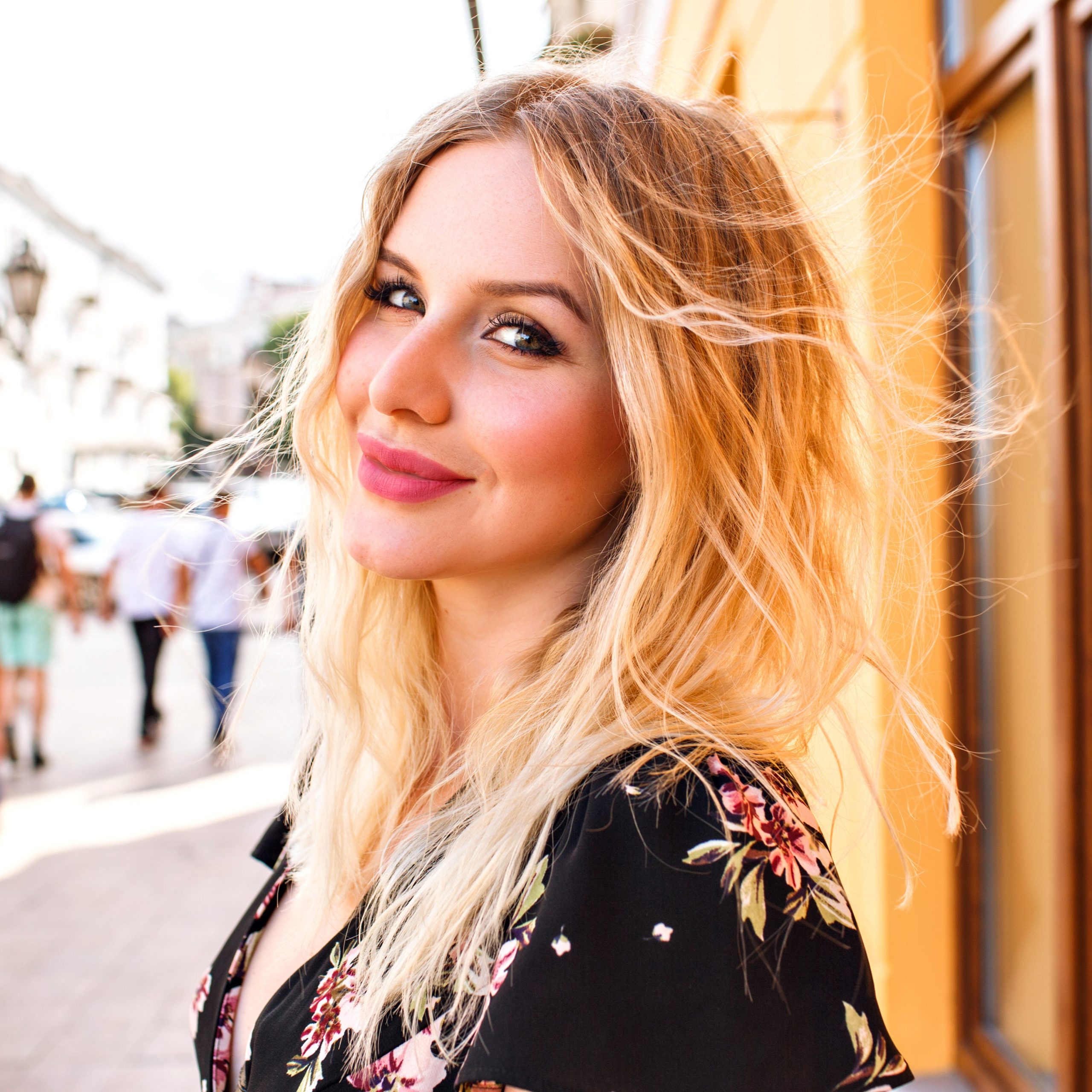 pretty blonde woman wearing floral dress posing near yellow wall scaled